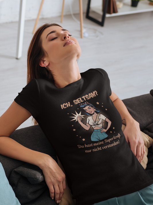 Frau, auf Sofa liegend, trägt schwarzes T-Shirt mit Motiv: Retro-Girl mit Text „Ich, seltsam? Du hast nur meine Superkraft nicht verstanden!“