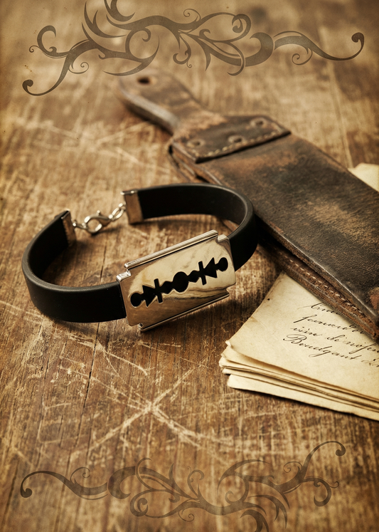 Schwarzes Razor Armband mit metallischer Klingenform auf Holztisch neben altem Ledermäppchen und Papierstapel.