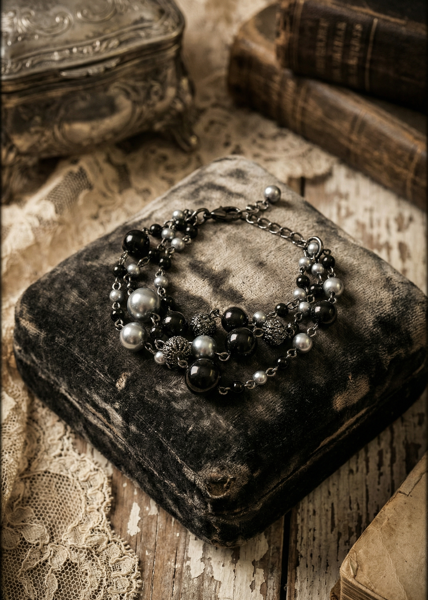 Dreifach geführtes Perlenarmband in Schwarz und Silber auf dunklem Samtkissen fotografiert