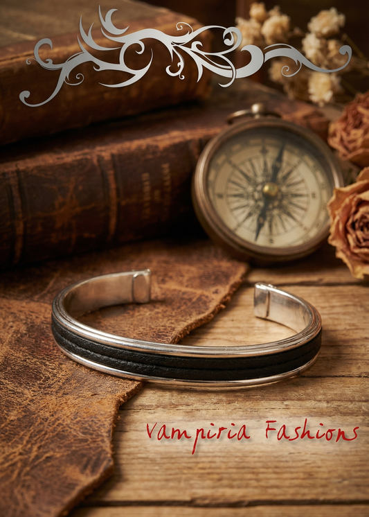 Silberfarbene offene Armspange mit schwarzem Mittelstreifen auf Holzoberfläche, dekoriert mit Büchern und Kompass im Vintage-Stil