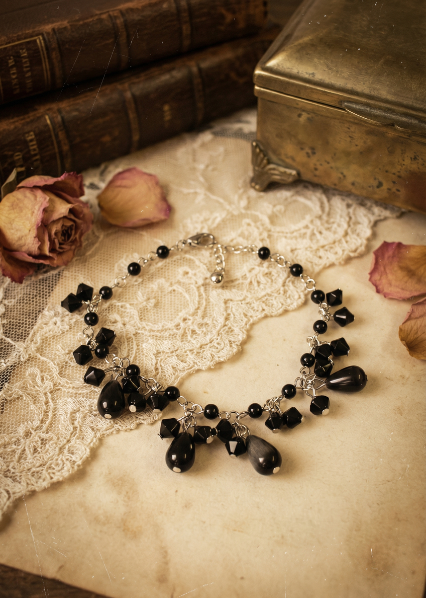 Gothic Armkettchen mit schwarzen Perlen und kleinen Anhängern, dekorativ auf hellem Untergrund neben Vintage-Dekoration fotografiert.