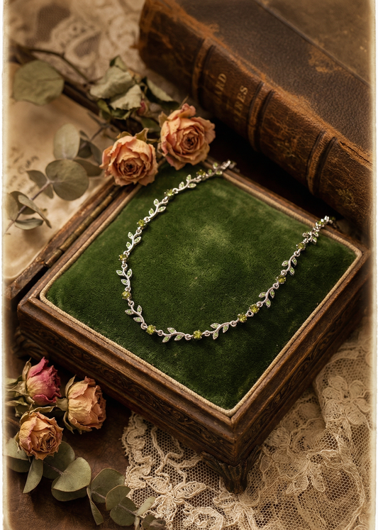 Filigranes silberfarbenes Collier mit grünen Kristallen in Blattform auf grünem Samtkissen in einer Vintage-Schmuckbox.
