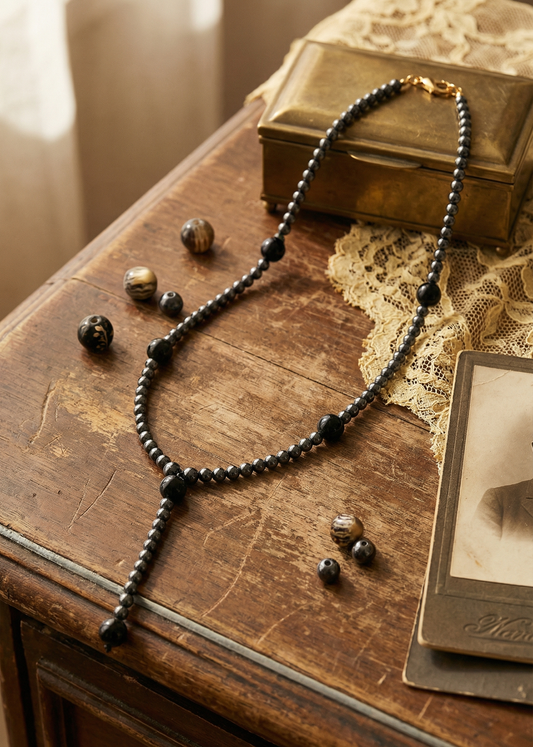 Langes Hämatit Collier liegend auf Holztisch mit dunklen Perlen und dekorativen Steinen