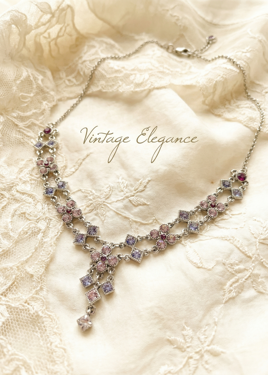 Silberfarbenes Vintage-Collier mit rosafarbenen und fliederfarbenen Strasssteinen auf cremefarbenem Stoff mit Schriftzug „Vintage Elegance“.