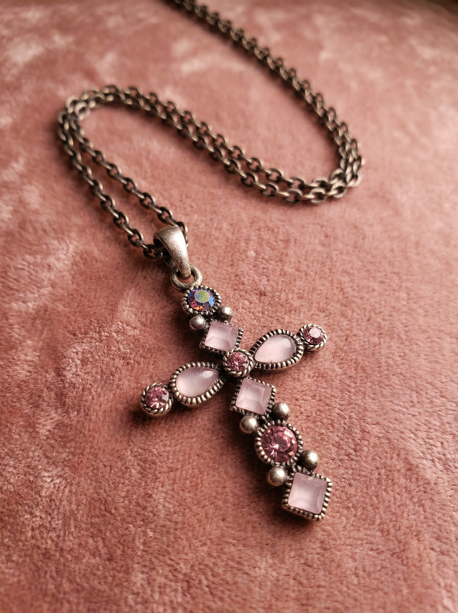 Kreuzanhänger im Antikdesign mit rosa und roséfarbenen Steinen an dunkler Gliederkette auf rosafarbenem Samtstoff.