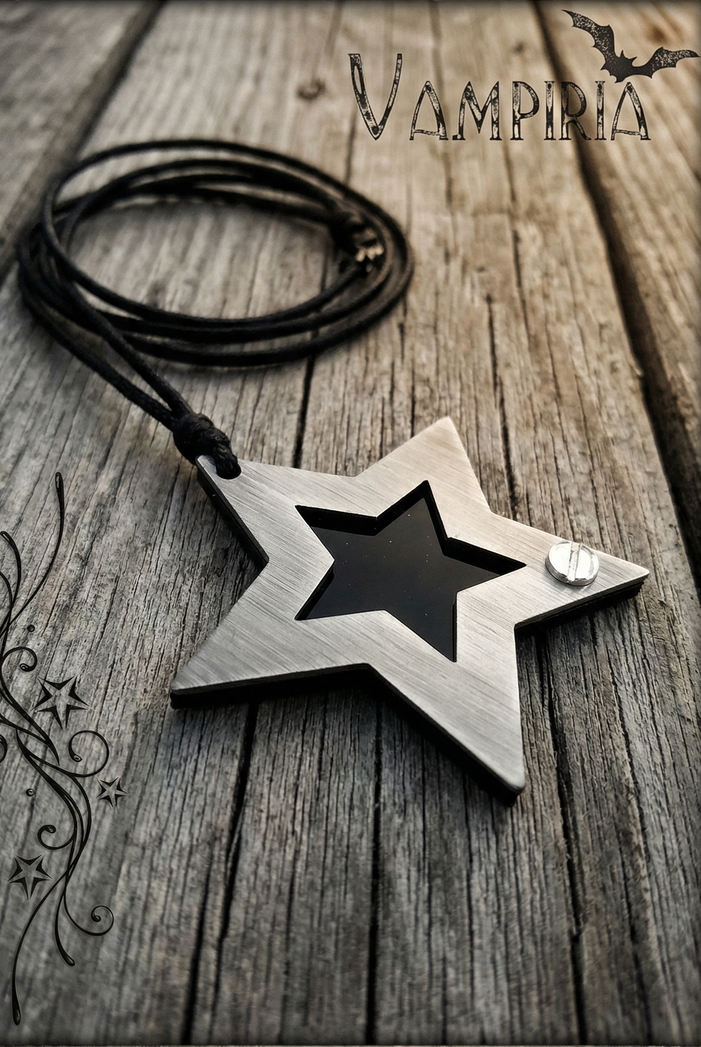 Sternförmiger Metallanhänger mit schwarzem Einsatz und schwarzem Band auf heller Holzoberfläche, oben Vampiria-Schriftzug und links Ornamentgrafik.