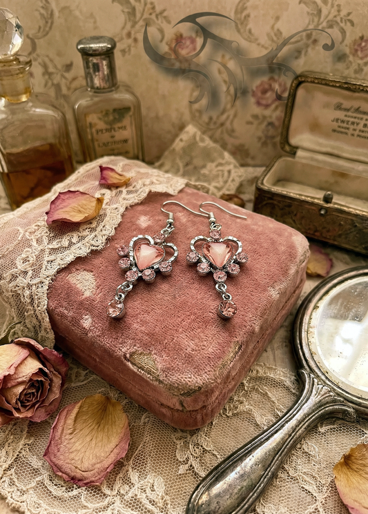 Rosa Herz-Ohrringe im Vintage-Stil auf rosafarbener Samtbox mit Spitze, Rosenblättern und alten Flakons