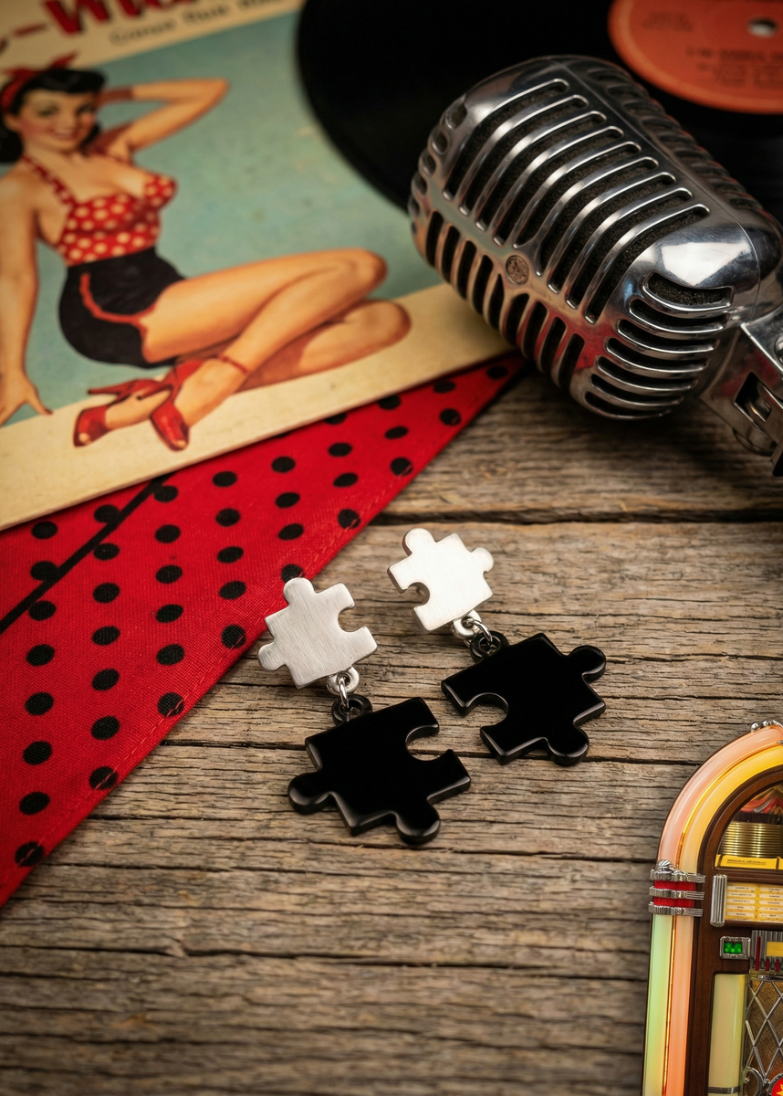 Zweifarbige Puzzle-Ohrstecker mit silberfarbenem oberen Puzzleteil und schwarzem hängendem Puzzleteil auf rustikalem Holztisch im Rockabilly-Setting mit Mikrofon und Schallplatte.