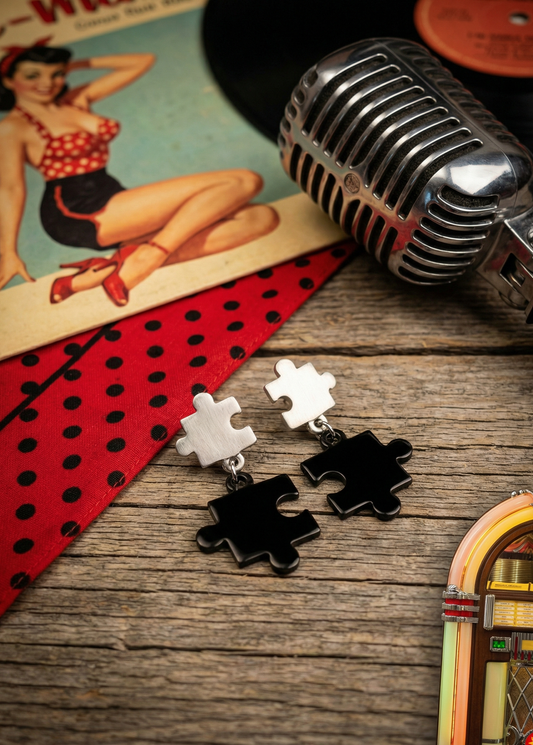 Zweifarbige Puzzle-Ohrstecker mit silberfarbenem oberen Puzzleteil und schwarzem hängendem Puzzleteil auf rustikalem Holztisch im Rockabilly-Setting mit Mikrofon und Schallplatte.