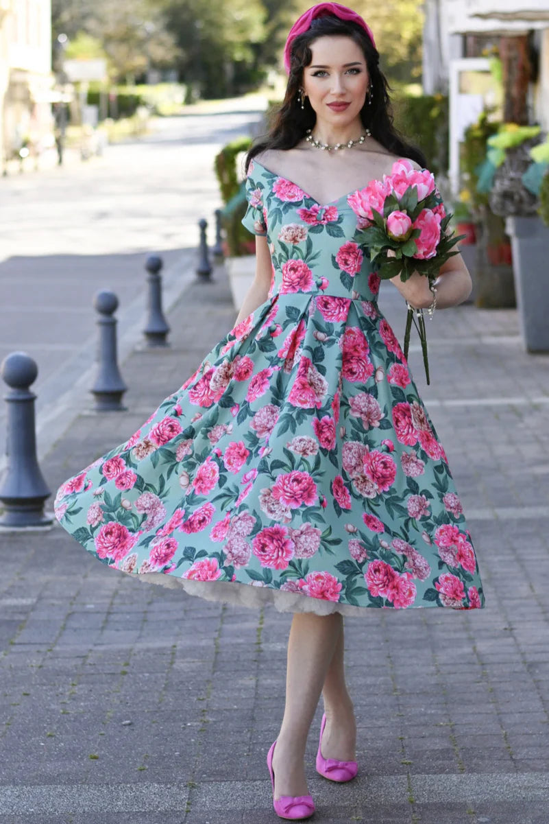 Frau trägt mintfarbenes Off-Shoulder Kleid mit rosa Pfingstrosen-Print und schwingendem Rock im 50er-Jahre-Stil.