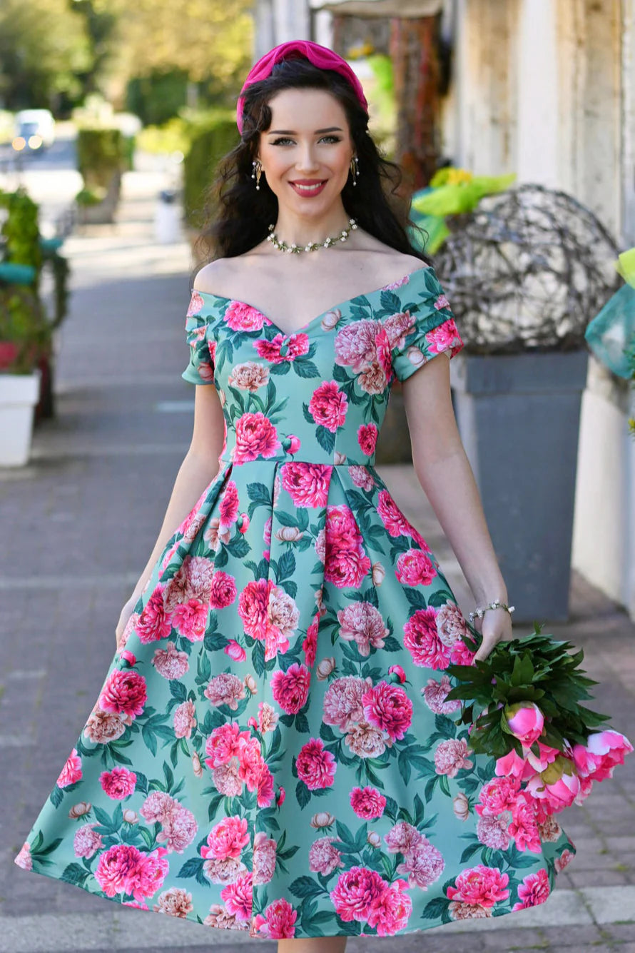 Frau trägt mintfarbenes Off-Shoulder Kleid mit rosa Pfingstrosen-Print und schwingendem Rock im 50er-Jahre-Stil.