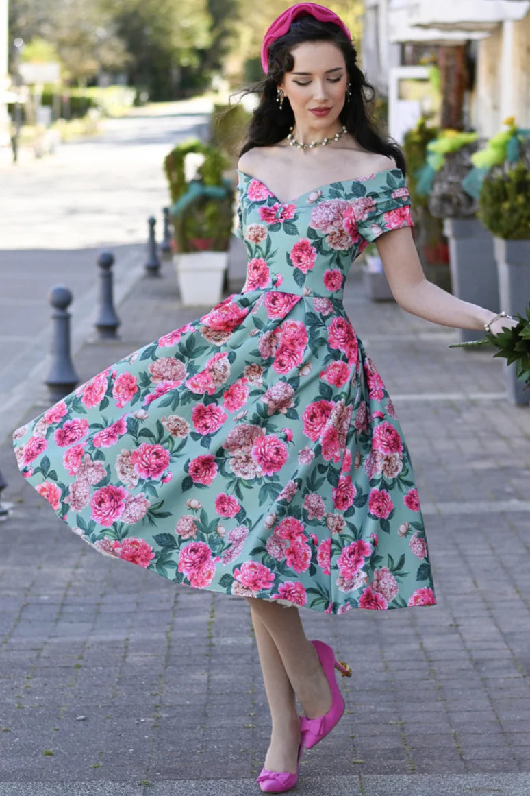 Frau trägt mintfarbenes Off-Shoulder Kleid mit rosa Pfingstrosen-Print und schwingendem Rock im 50er-Jahre-Stil.