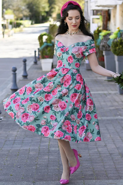 Frau trägt mintfarbenes Off-Shoulder Kleid mit rosa Pfingstrosen-Print und schwingendem Rock im 50er-Jahre-Stil.