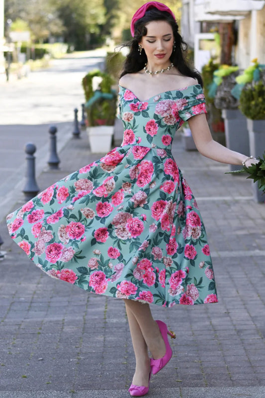 Frau trägt mintfarbenes Off-Shoulder Kleid mit rosa Pfingstrosen-Print und schwingendem Rock im 50er-Jahre-Stil.