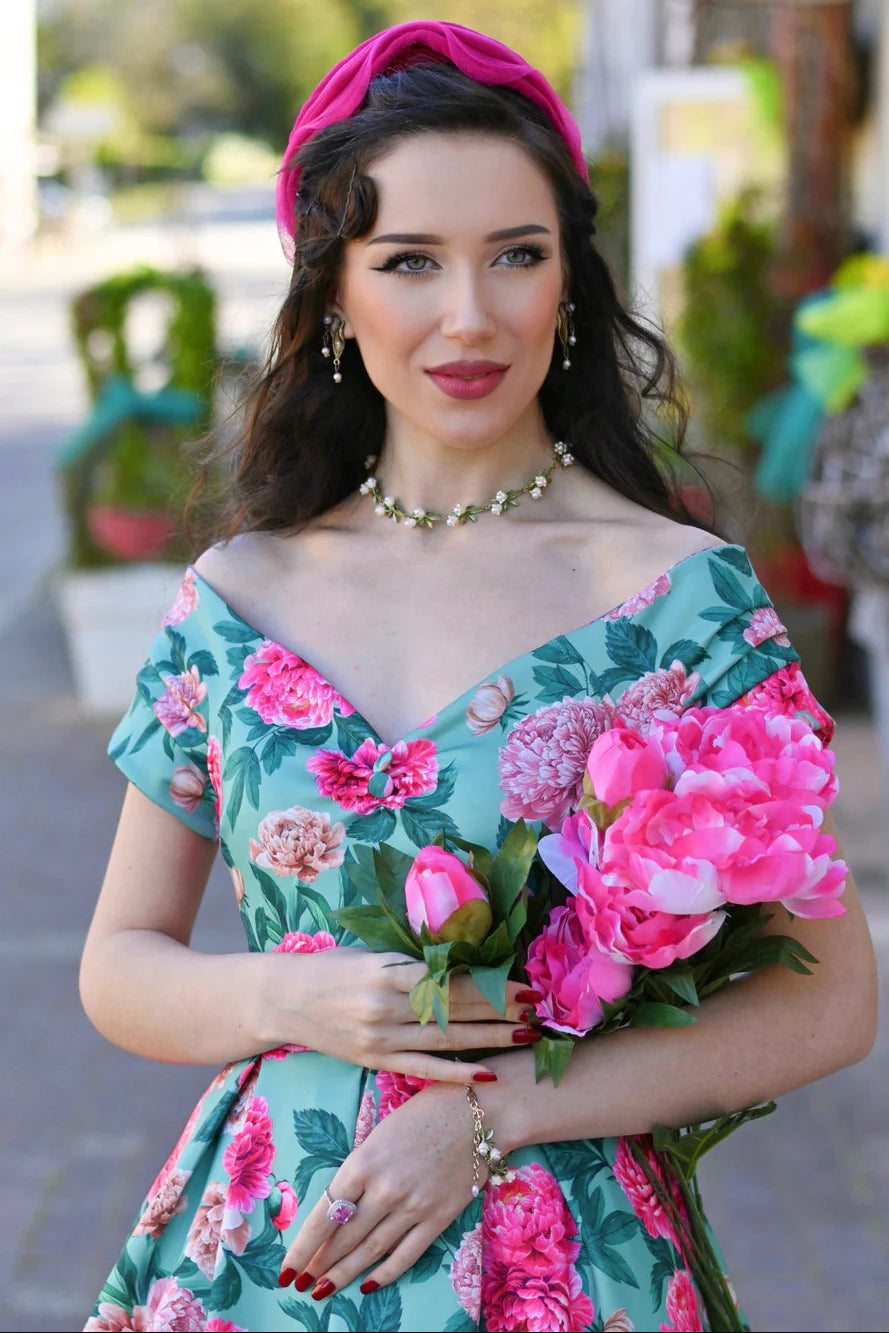 Frau trägt mintfarbenes Off-Shoulder Kleid mit rosa Pfingstrosen-Print und schwingendem Rock im 50er-Jahre-Stil.