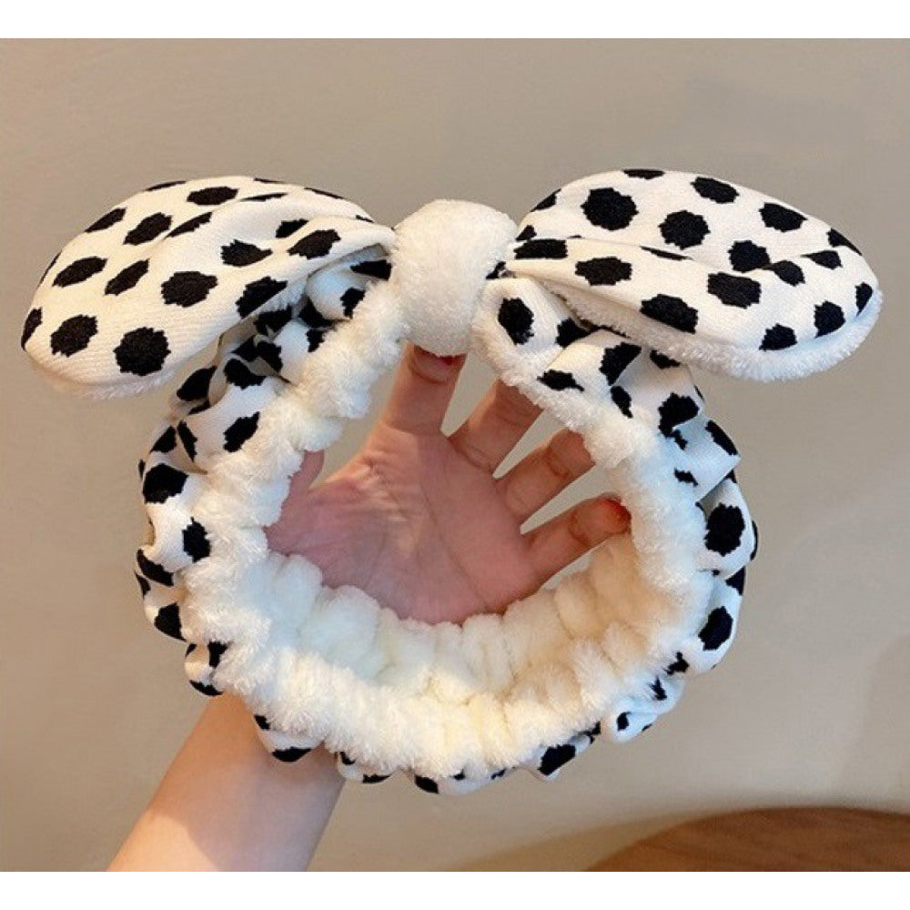 Flauschiger Kosmetik-Haarreif in Weiß mit schwarzen Leo-Flecken und Schleifen-Detail auf hellem Hintergrund mit Hand