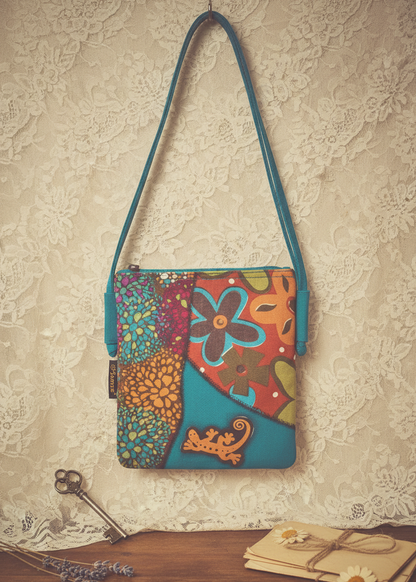 Bunte Patchwork-Schultertasche aus Baumwolle mit floralem Muster und blauem Trageriemen vor hellem Hintergrund.