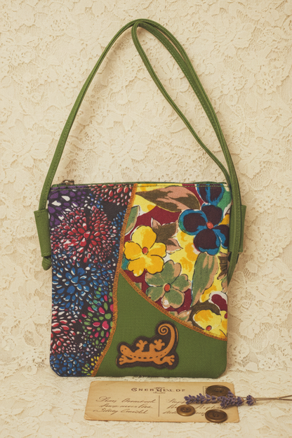 Bunte Patchwork-Schultertasche aus Baumwolle mit floralem Muster und grünem Trageriemen auf Holztisch.