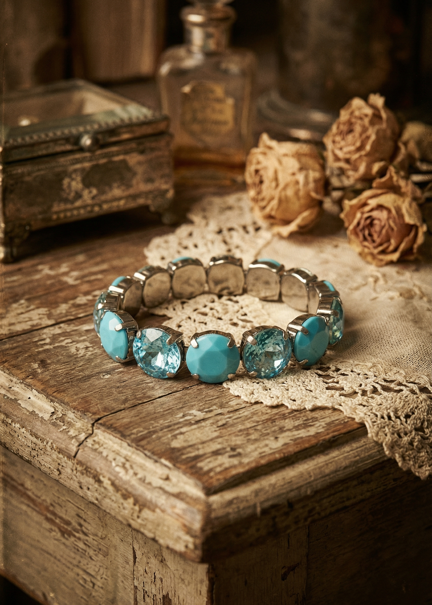 Türkisfarbenes Armband mit runden Schmucksteinen auf heller Spitze und Vintage-Dekoration.
