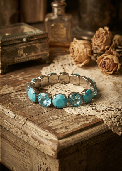 Türkisfarbenes Armband mit runden Schmucksteinen auf heller Spitze und Vintage-Dekoration.