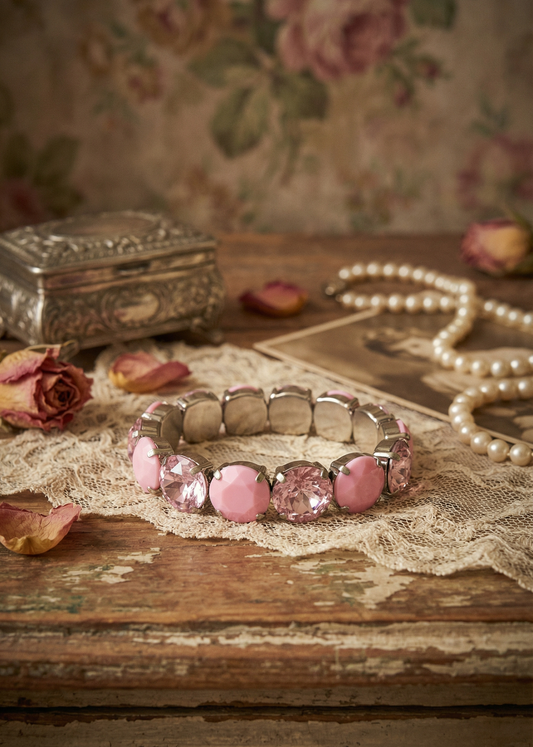 Rosa Vintage Armband mit facettierten und glatten Schmucksteinen auf Spitze und Holzuntergrund.