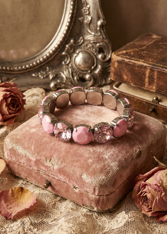 Rosa elastisches Armband mit funkelnden Kristallsteinen auf rosafarbenem Samtkissen im Vintage-Stil.