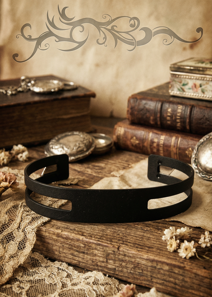 Schwarze minimalistische Metall-Armspange auf rustikalem Holztisch mit Vintage-Dekoration.