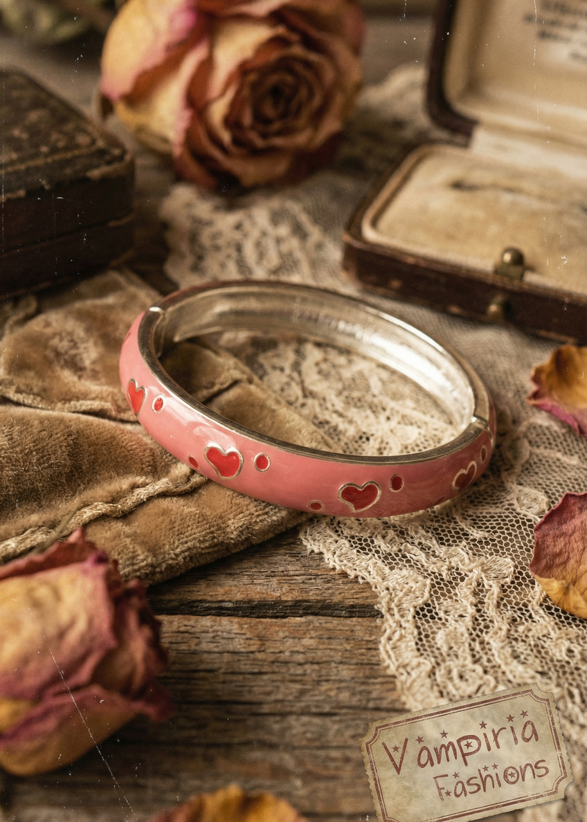 Rosa Armspange mit kleinen Herzen auf Stoffuntergrund neben Vintage-Dekoration.