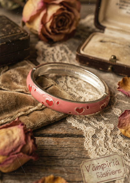 Rosa Armspange mit kleinen Herzen auf Stoffuntergrund neben Vintage-Dekoration.