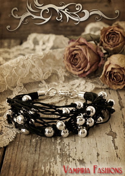 Mehrreihiges schwarzes Gothic Armkettchen mit silberfarbenen Perlen auf rustikalem Holztisch mit Spitzenstoff und getrockneten Rosen.