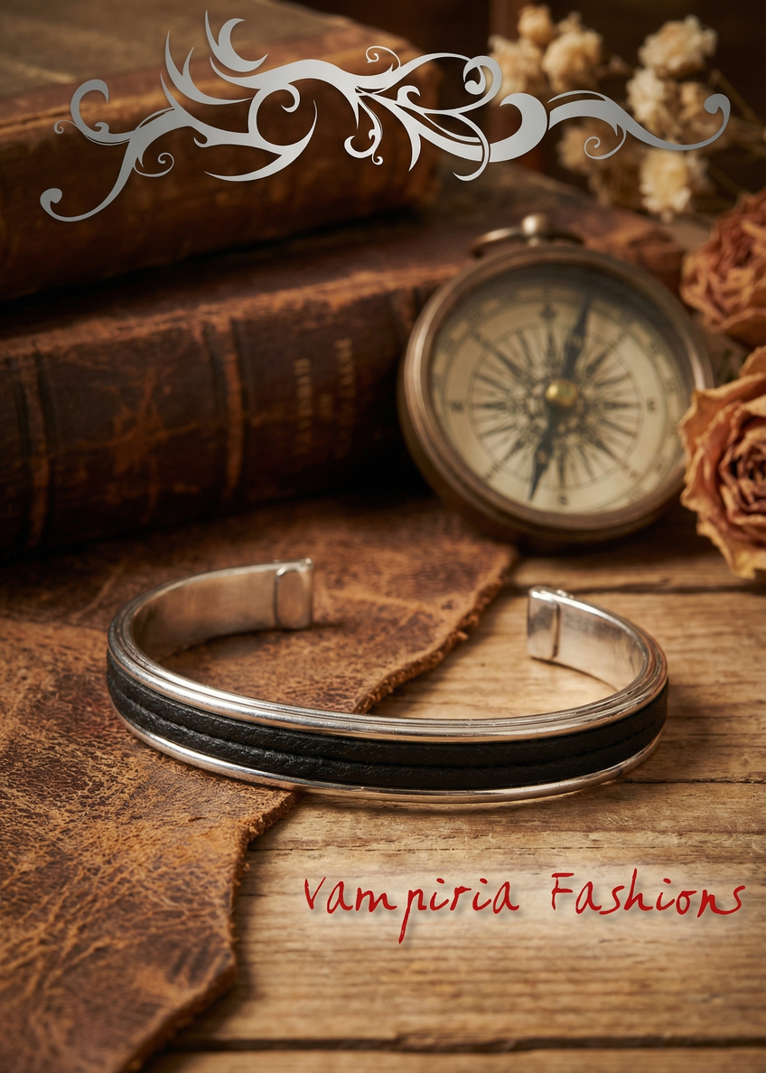 Silberfarbene offene Armspange mit schwarzem Mittelstreifen auf Holzoberfläche, dekoriert mit Büchern und Kompass im Vintage-Stil