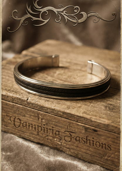 Schlichte silberfarbene Armspange mit schwarzem Einsatz auf Holzkiste im Vintage-Gothic Ambiente.
