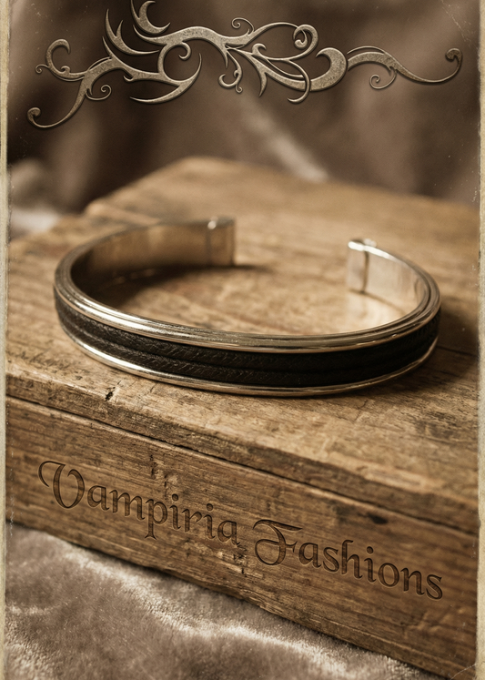 Schlichte silberfarbene Armspange mit schwarzem Einsatz auf Holzkiste im Vintage-Gothic Ambiente.
