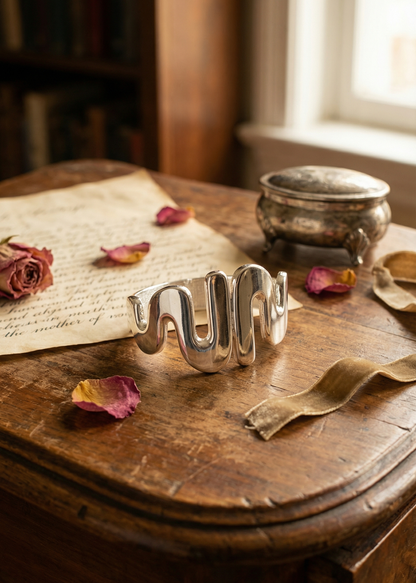 Silberfarbene Armspange mit geschwungenem Design auf Holztisch mit Vintage-Dekoration.