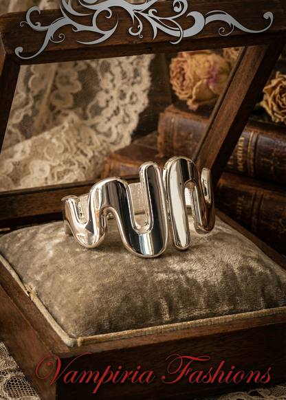 Silberfarbene Armspange in wellenförmiger Form auf Samtkissen in Holzbox.