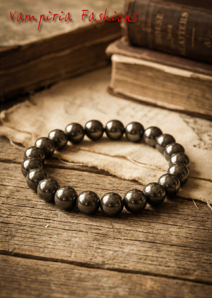 Hämatit-Perlenarmband mit dunklen, runden Perlen auf rustikalem Holztisch neben alten Büchern.