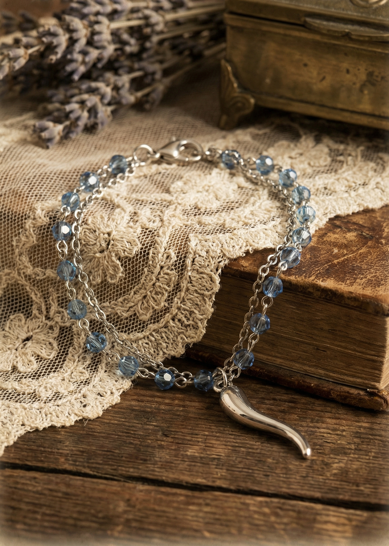 Doppeltes silberfarbenes Armkettchen mit blauen Glasperlen und Anhänger auf Holzoberfläche.