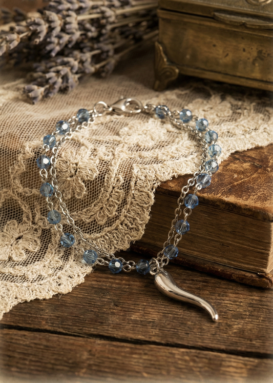 Doppeltes silberfarbenes Armkettchen mit blauen Glasperlen und Anhänger auf Holzoberfläche.