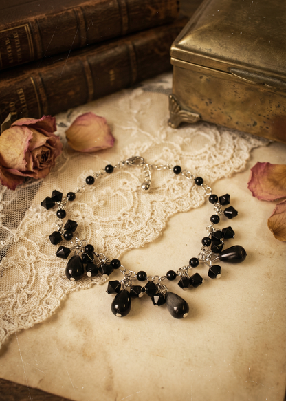 Gothic Armkettchen mit schwarzen Perlen und kleinen Anhängern, dekorativ auf hellem Untergrund neben Vintage-Dekoration fotografiert.