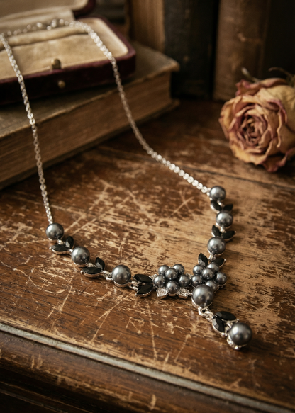 Dunkles Collier mit Perlen und schwarzen Schmuckelementen liegt auf rustikalem Holztisch vor Büchern und getrockneter Rose.