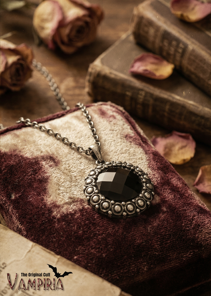 Nahaufnahme einer Gothic Kette mit facettiertem schwarzem Medaillon auf Stoffuntergrund.