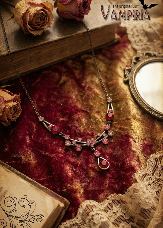 Vintage Gothic Collier mit roten und rosafarbenen Kristallen auf samtigem Stoff neben Spiegel und alten Büchern.