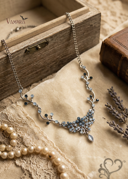 Blaues Kristall-Collier mit floralem Design auf Stoffuntergrund neben Holzbox, Buch und Lavendelzweigen.