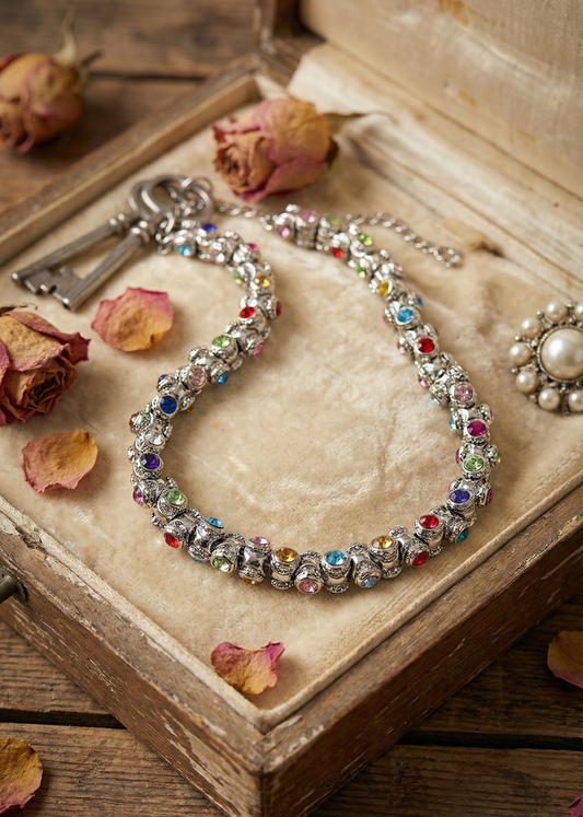 Vintage Collier mit farbigen Steinen liegt in einer geöffneten Schmuckbox mit getrockneten Rosen.
