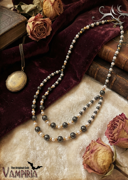 Zweireihiges Collier mit feinen verschiedenfarbigen Kunststoffperlen und goldfarbenen Elementen auf Stoff mit Rosen im Vintage-Stil.