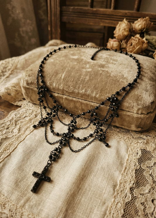 Schwarzer Gothic Choker mit Kreuzanhänger auf hellem Samtkissen mit Spitzenstoff im Vintage-Setting.