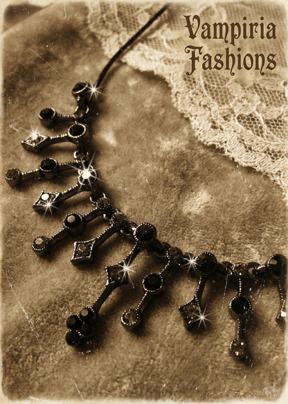 Detailaufnahme eines schwarzen Gothic-Colliers mit funkelnden Strasssteinen und ornamentalem Anhängerbereich auf samtigem Stoff.