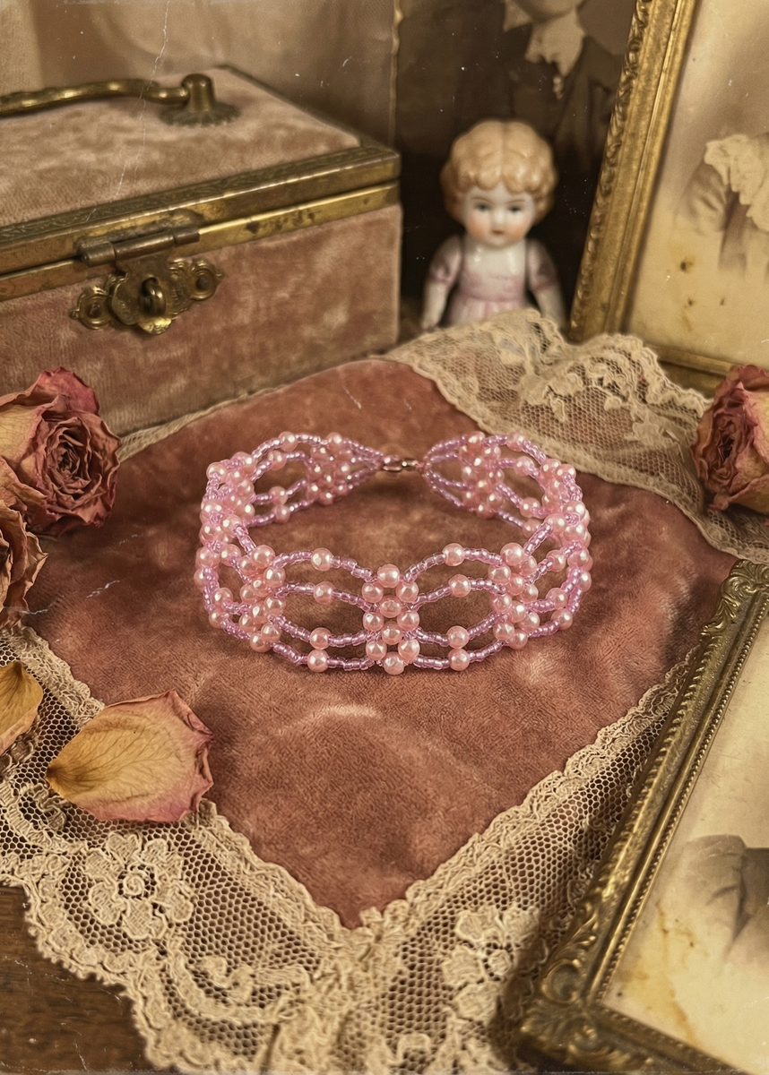 Rosa Perlen-Choker mit mehrreihigem Muster auf rosa Samtkissen, umgeben von Spitze, Trockenrosen und Vintage-Dekoration.