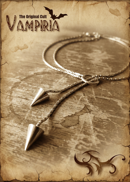 Silberfarbene Pendel-Kette mit zwei Kegelspitzen auf Holzoberfläche im Vintage-Stil mit Vampiria-Logo.