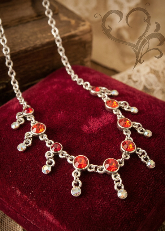 Rotes Collier mit silberfarbener Fassung und roten sowie klaren Schmucksteinen auf rotem Samtkissen.